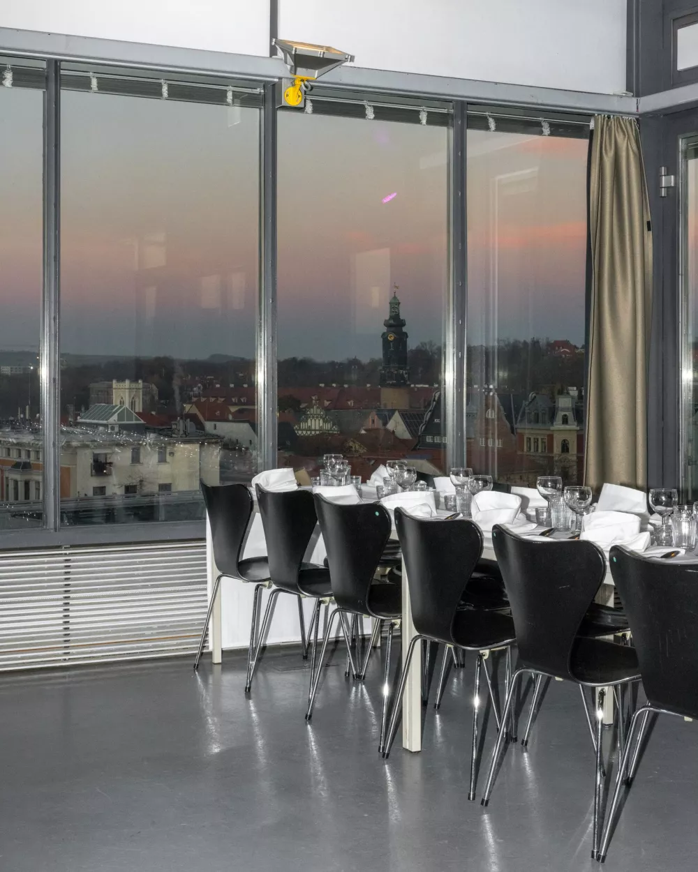 ein Zimmer in einem hohen Gebäude mit einem langen Esstisch, aus dem man den Sonnenuntergang sehen kann