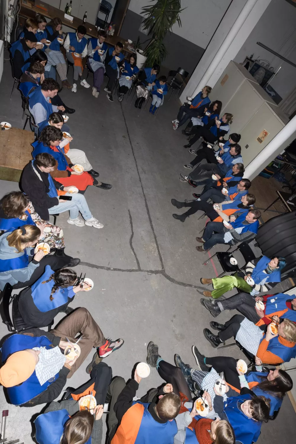 zahlreiche Menschen, die in einer kreisförmigen Anordnung zusammensitzen und gemeinsam essen