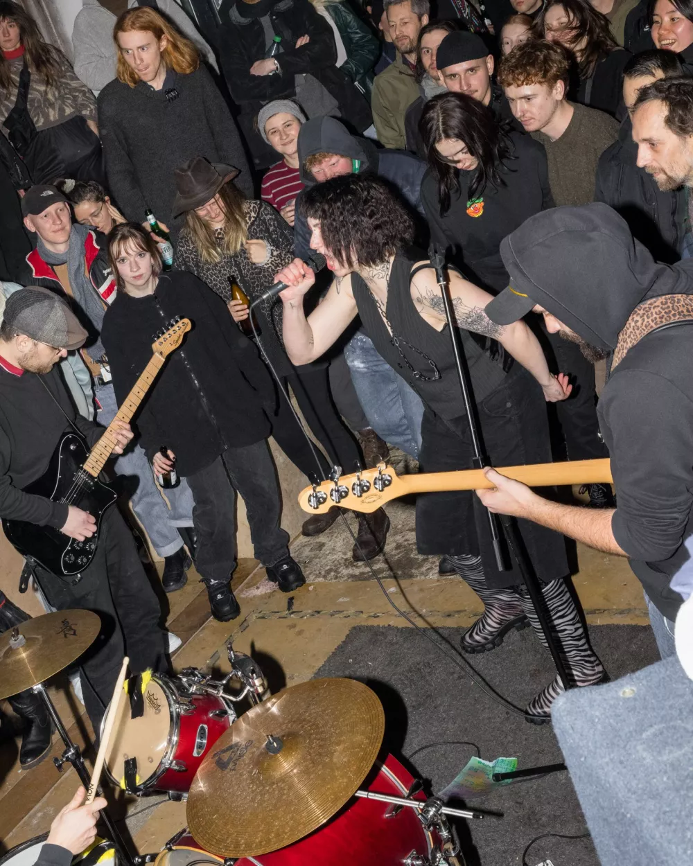 ein Veranstaltungsraum, der mit einer großen Anzahl von Besucher*innen gefüllt ist und in dessen Mitte eine Band spielt