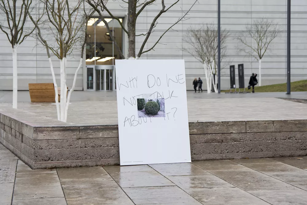 eine an eine Betonsitzgruppe gelehnte Tafel mit der Aufschrift „Why do we not talk about it?“ (z.Dt.: 