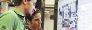 Two people in front of a monitor with measurement results from a test.