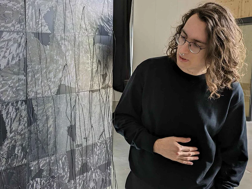 Timon Bohn looking at a large-format black-and-white graphic work with fine linear structures and wires hanging from it.