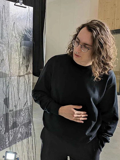 Timon Bohn looking at a large-format black-and-white graphic work with fine linear structures and wires hanging from it.