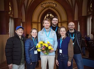 Florian Wehking (Mitte) mit Blumenstrauß und Urkunde für seinen Film »Arbeiter betreten die Fabrik« gemeinsam mit den Juror*innen.