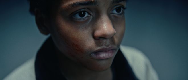 Film still from »DROWNING IS SILENT« by Alexander Knauer: close-up of a boy with a serious expression and visible marks on his face.