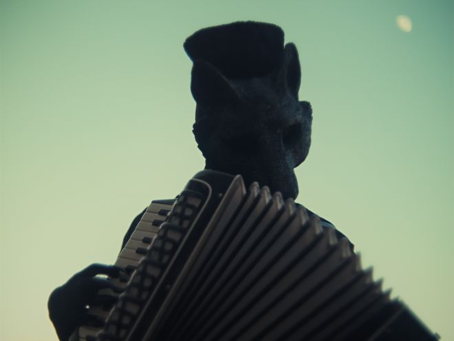 Person mit tierförmigem Kopf spielt ein Akkordeon im Gegenlicht.