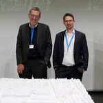 Zwei Männer stehen hinter einem Architekturmodell.