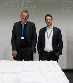 Zwei Männer stehen hinter einem Architekturmodell.