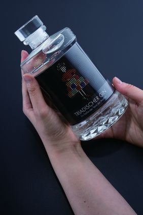 »TRIADISCHER GIN« by Xiaoyi Jin, Photo: Xiaoyi Jin Detail view of »TRIADISCHER GIN« by Xiaoyi Jin: two hands hold a gin bottle with a lenticular label. The label shows an abstract, colourful figure that appears to move when the bottle is turned.