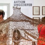 Detail der Ausstellung »Was bleibt – Ein familiäres Archiv«: Eine weit ausladende Installation aus braunen Tonbändern hängt im Ausstellungsraum, im Hintergrund sind Besucher*innen und Dokumente der »Aktion Ungeziefer« zu sehen.