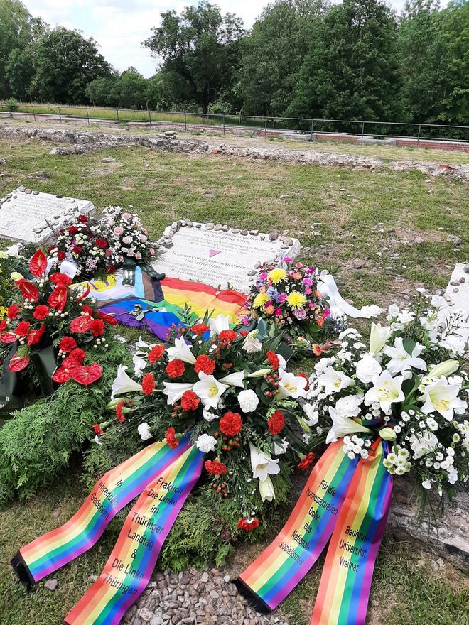 The photo shows various flower arrangements at the memorial stone for the homosexual men imprisoned and murdered by the Nazis in the Buchenwald and Mittelbau-Dora concentration camps. The memorial plaque bears the inscription (in German and English): »In memory of the homosexual men that suffered here / There were 650 Rosa Winkel prisoners in the Buchenwald concentration camp between 1937 – 1945. Many of them lost their lives«.