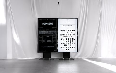 Transforming Voice into Dynamic Fonts Two monitors standing side by side in front of a white fabric background. On the left, a dark interface from VOXAIPE; on the right, a light-coloured page with generated letter shapes.