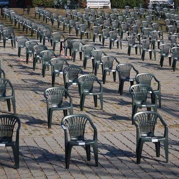 Numerous dark grey plastic monobloc chairs are arranged in regular rows on a paved outdoor area.