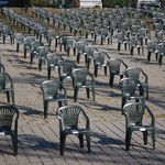 Photo: Adrian Bancu; Source: Pexels Numerous dark grey plastic monobloc chairs are arranged in regular rows on a paved outdoor area.