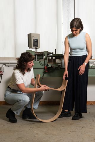 Mira Müller und Mara Trübenbach mit einem Objekt aus gebogenem Holz in einer Werkstatt