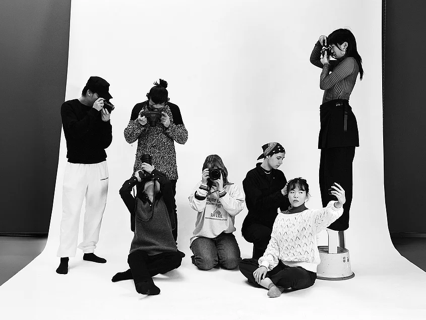 »Beyond the Lightmeter«: Sieben Personen in einem Fotostudio vor weißem Hintergrund. Mehrere fotografieren mit Kameras, eine Person im Vordergrund hält ein Smartphone für ein Selfie. Foto: Julia Albrecht