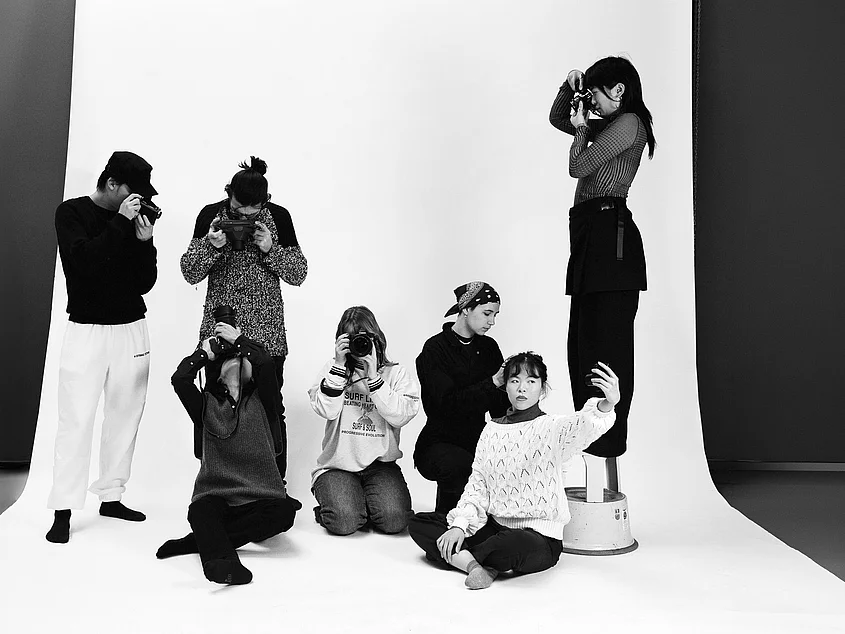 »Beyond the Lightmeter«: Seven people in a photo studio against a white backdrop. Several are taking pictures with cameras, while one person in the foreground holds up a smartphone for a selfie. Photo: Julia Albrecht