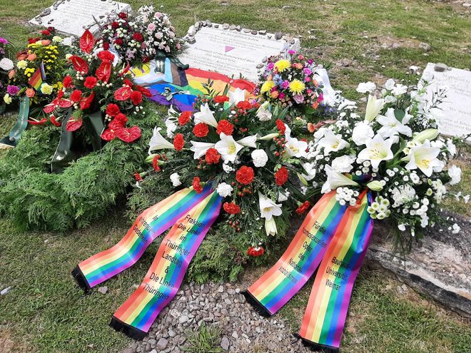 The photo shows various flower arrangements at the memorial stone for the homosexual men imprisoned and murdered by the Nazis in the Buchenwald and Mittelbau-Dora concentration camps. The memorial plaque bears the inscription (in German and English): »In memory of the homosexual men that suffered here / There were 650 Rosa Winkel prisoners in the Buchenwald concentration camp between 1937 – 1945. Many of them lost their lives«.