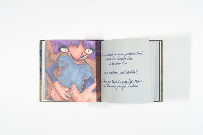 Open picture book with a colourful illustration on the left and handwritten text on the right. The illustration shows a figure with a round belly and blue clothing.