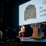 Laura Wiemers sitzt auf einer Bühne und hält ein Buch in der Hand, aus dem sie liest