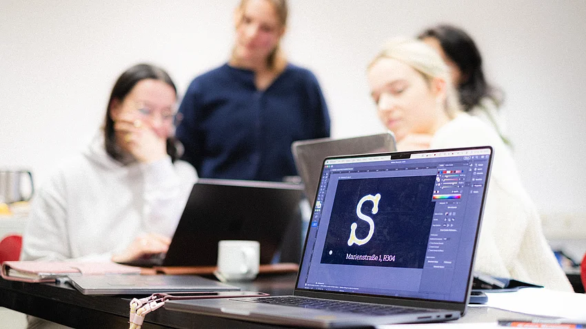 mehrere Personen sitzen zusammen an Tischen und arbeiten am Laptop
