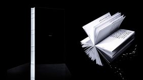 Book view of »VOXAIPE – Decoded«, Photo: Mai Do Book view of »VOXAIPE – Decoded« by Mai Do: a black volume and an opened artist’s book are shown against a dark background. The open pages display variable letterforms derived from vocal characteristics.