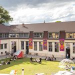 People in the courtyard in front of the Van de Velde building during summaery2024, with knitted textile banners hanging on the façade
