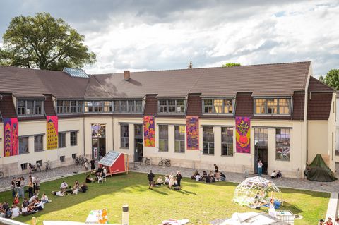 Projektpräsentationen, Plenen und Co.  Menschen im Innenhof vor dem Van-de-Velde-Bau während der summaery2024, an der Fassade hängen gestrickte textile Banner.