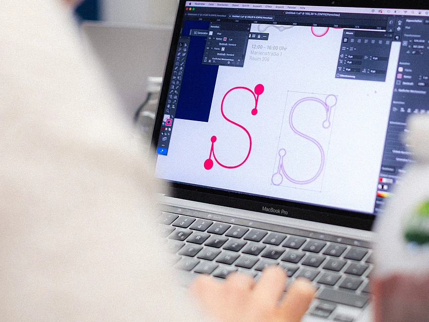 eine Person von hinten fotografiert, arbeitet an einer Schrift auf ihrem Laoptop