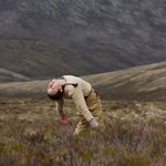 A woman is standing on a meadow and bends her upper body very strongly into a hollow back