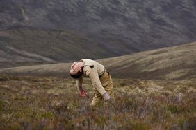 A woman is standing on a meadow and bends her upper body very strongly into a hollow back
