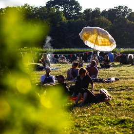 Szene vom Hörspielsommer: Wiese mit mit Menschen und gelbem Sonnenschirm in der Abendsonne; Foto: Tino Pfund