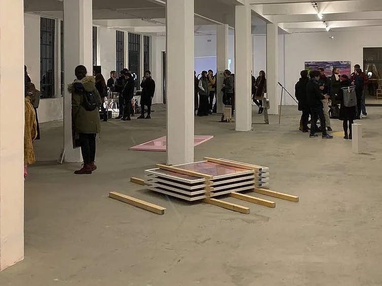 Ausstellungsansicht mit zahlreichen Besucher*innen und verschiedenen künstlerischen Arbeiten in einem weitläufigen Raum mit weißen Säulen.