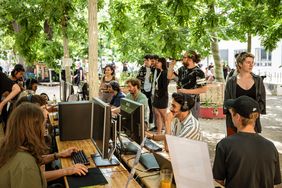 Im Garten der M18 ist ein Tisch mit Computern aufgebaut, an dem Studierende sitzen.