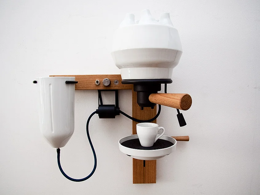 An der Wand montierte Espressomaschine aus weißem Porzellan und Holz mit Tasse auf der Abstellfläche.