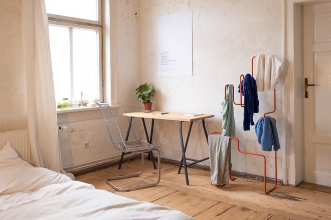 Photo of a room with the clothes on the clothes horse next to a desk.