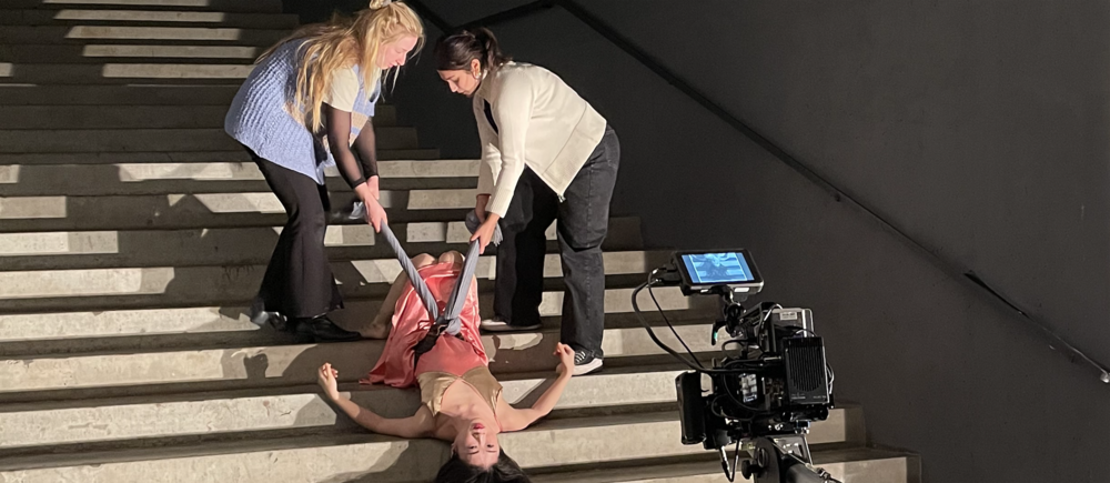 Foto von den Dreharbeiten zu einem der Filme: eine Tänzerin liegt kopfüber auf einer Treppe und wird dabei von oben gefilmt