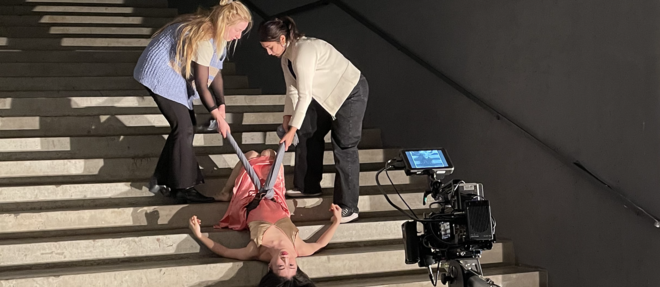 Foto von den Dreharbeiten zu einem der Filme: eine Tänzerin liegt kopfüber auf einer Treppe und wird dabei von oben gefilmt 