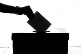 Das Foto zeigt eine Hand, die einen Wahlzettel in eine Wahlbox einwirft.