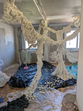 Rauminstallation aus schaumartigem Material, die sich verzweigt im Raum ausbreitet, in einem unfertigen Innenraum