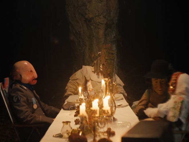 Mehrere Personen sitzen an einem Tisch im Wald, beleuchtet von Kerzen.