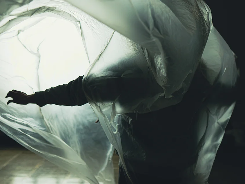 A person moves through a large translucent sheet that billows around their body. Light shines through the material, outlining the person as a silhouette.