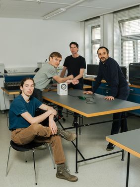 Foto des Forschungsteams an einem Tisch. Darauf liegt ein Prototyp des neuen Saitentyps.