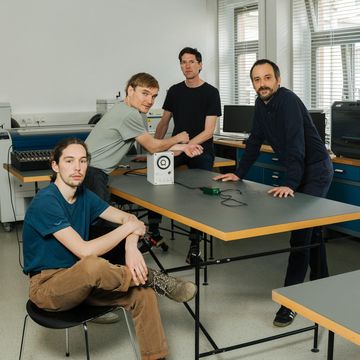 Photo of the research team at a table. A prototype of the new type of string lies on it.