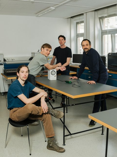 Future musical instruments without resonators and pickups possible Photo of the research team at a table. A prototype of the new type of string lies on it.