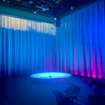 Bunt erleuchteter Raum, der durch Vorhänge im Hintergrund begrenzt wird. Ein Schlaglicht ist auf ein kleines Radio am Boden gerichtet