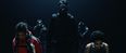 Film still from »DROWNING IS SILENT« by Alexander Knauer: a sea rescuer and a boy stand in the foreground with lowered gazes. Behind them, dark-clad figures wearing gas masks approach.