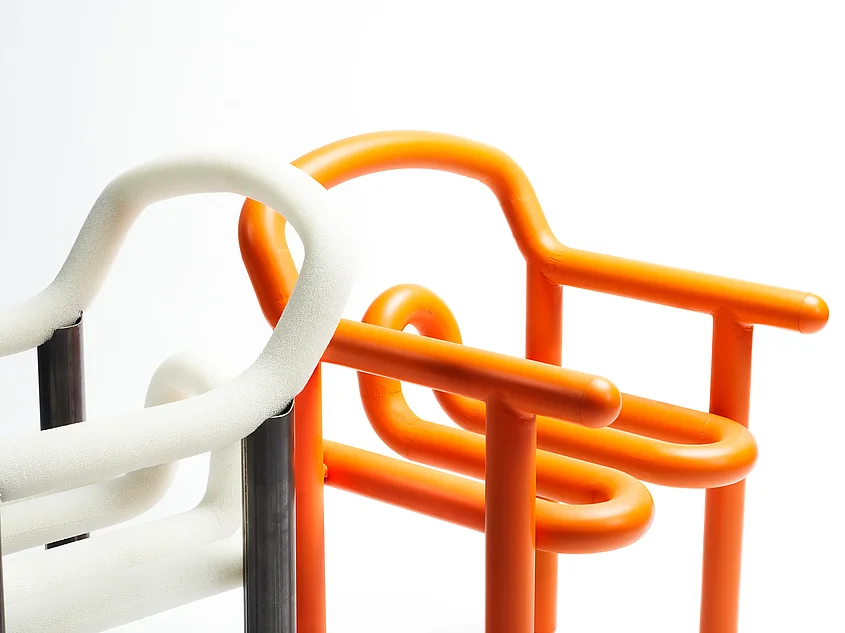 Detail des Pflegeduschstuhls LAVA mit geschwungenen orangefarbenen und weißen Rohrelementen vor weißem Hintergrund.