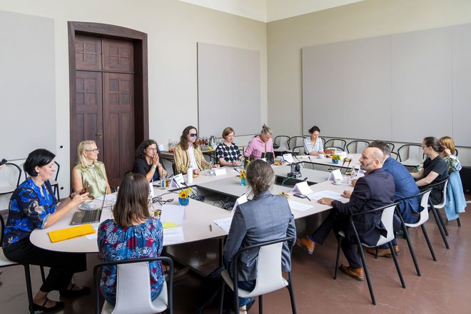 Ein elipsenförmiger Besprechungstisch füllt den ganzen Raum aus. 13 Personen sitzen an diesem und hören interessiert zu, sie sind positiv gestimmt. 