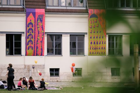 Jetzt informieren! Studierende sitzen auf der Wiese vor dem Van-de-Velde-Bau; am Gebäude hängt ein farbenfrohes Banner aus Textil